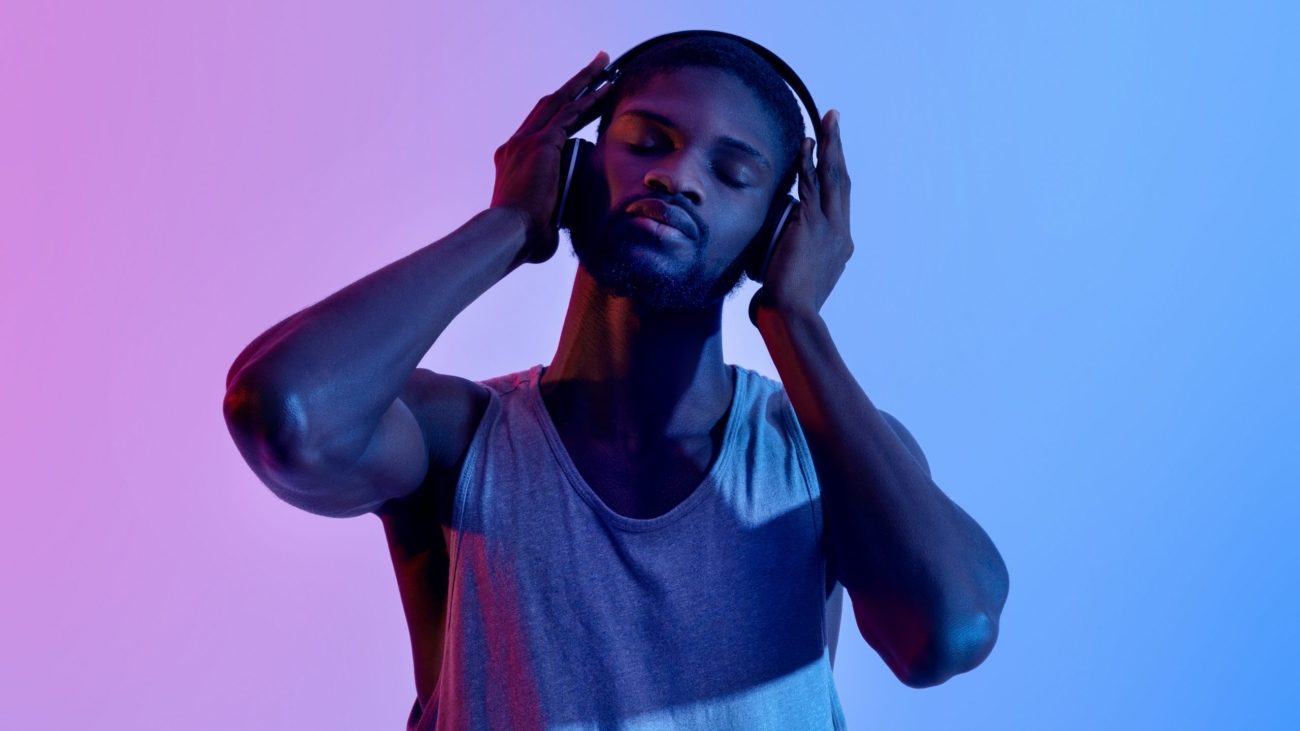 Peaceful black athlete listening to music in headphones on break from his training in neon light. Funky African American sportsman enjoying favorite playlist with closed eyes